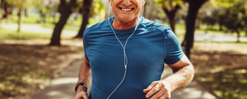 Portrait of a senior man in fitness wear running in a park. Close up of a smiling man running while listening to music using earphones.